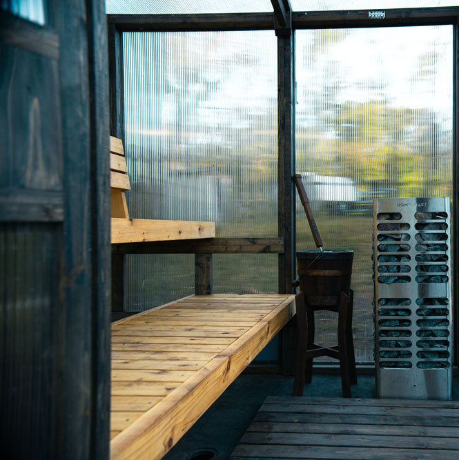 Sauna by Soluna with cedar wooden benches and a chair, glass walls, and a wooden shelf.